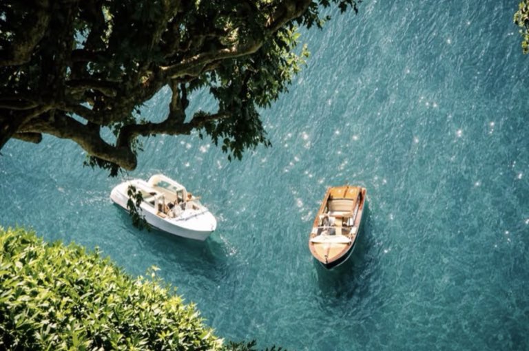 Two wooden boats on clear turquoise water beneath an overhanging tree